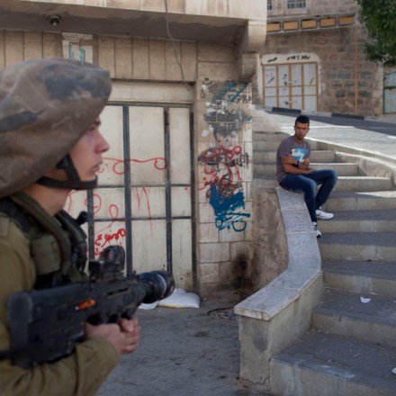 HEBRON, WEST BANK - SEPTEMBER 23: (ISRAEL OUT) Palestinians watch an Israeli soldier on patrol in a street on September 23, 2013 in Hebron, West Bank. Israeli security forces showed strong presence in Hebron following the incident in which a Palestinian sniper shot dead an Israeli soldier September 22 and thousands of Jewish visitors come to pray at the Cave of the Patriarchs for the Sukkot holday. (Photo by Lior Mizrahi/Getty Images)