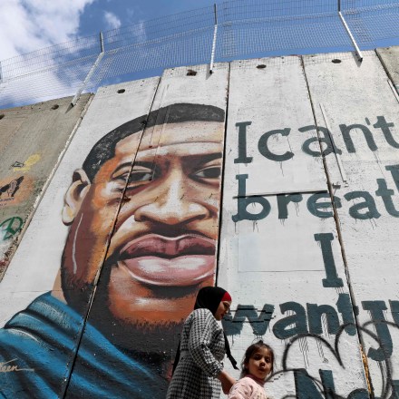 People walk past a mural showing the face of George Floyd, an unarmed handcuffed black man who died after a white policeman knelt on his neck during an arrest in the US, painted on a section of Israel's controversial separation barrier in the city of Bethlehem in the occupied West Bank on March 31, 2021. - The teenager who took the viral video of George Floyd's death said on March 30, at the trial of the white police officer charged with killing the 46-year-old Black man that she knew at the time "it wasn't right." Darnella Frazier, 18, was among the witnesses who gave emotional testimony on Tuesday at the high-profile trial of former Minneapolis police officer Derek Chauvin. Chauvin, 45, is charged with murder and manslaughter for his role in Floyd's May 25, 2020 death, which was captured on video by Frazier and seen by millions, sparking anti-racism protests around the globe. In the video, Chauvin, who was subsequently fired from the police department, is seen kneeling on the neck of a handcuffed Floyd for more than nine minutes. (Photo by Emmanuel DUNAND / AFP) (Photo by EMMANUEL DUNAND/AFP via Getty Images)