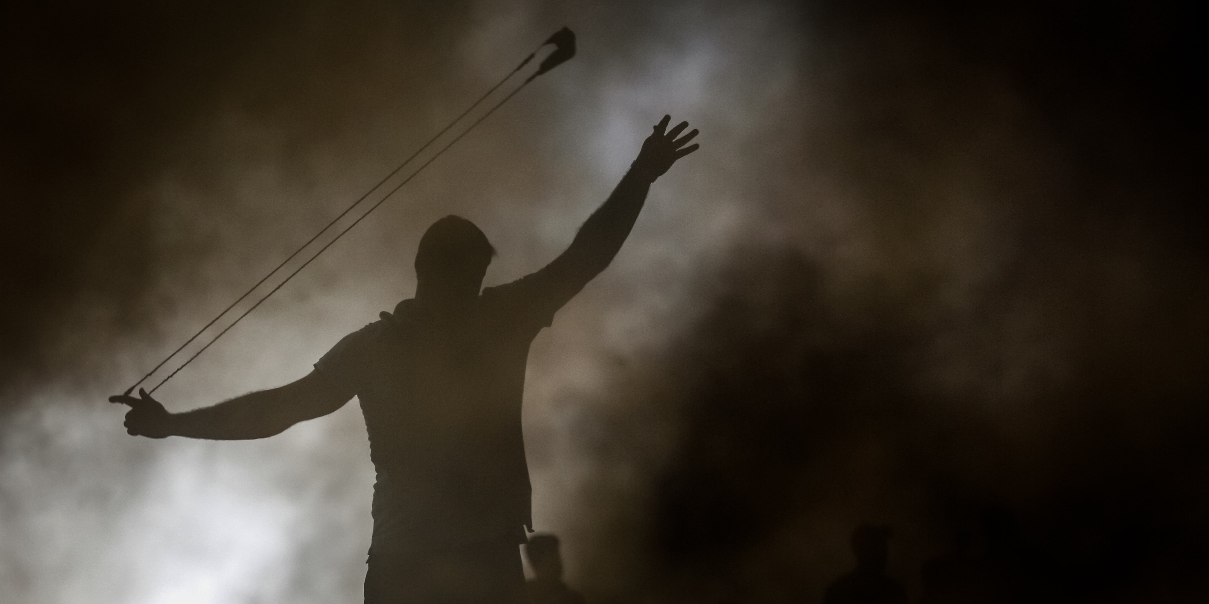 GAZA, PALESTINE - 2022/10/25: A Palestinian protester uses a slingshot to hurl stones during the protest against Israeli military raid in the West Bank, along the border fence with Israel, in east of Gaza City. The military says Israeli forces have raided a stronghold of an armed group in the West Bank, blowing up an explosives lab and engaging in a firefight. Palestinian health officials say five Palestinians were killed and 20 were wounded. The target of the raid was a group calling itself the Lions' Den, accused by Israel of having killed a soldier and attempting several attacks. (Photo by Ahmed Zakot/SOPA Images/LightRocket via Getty Images)