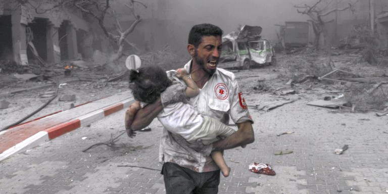 GAZA CITY, GAZA - OCTOBER 09: A medical worker rushes a child to the ambulance for treatment after Israeli airstrikes destroy buildings in Gaza City, Gaza on October 09, 2023. (Photo by Belal Khaled/Anadolu Agency via Getty Images)